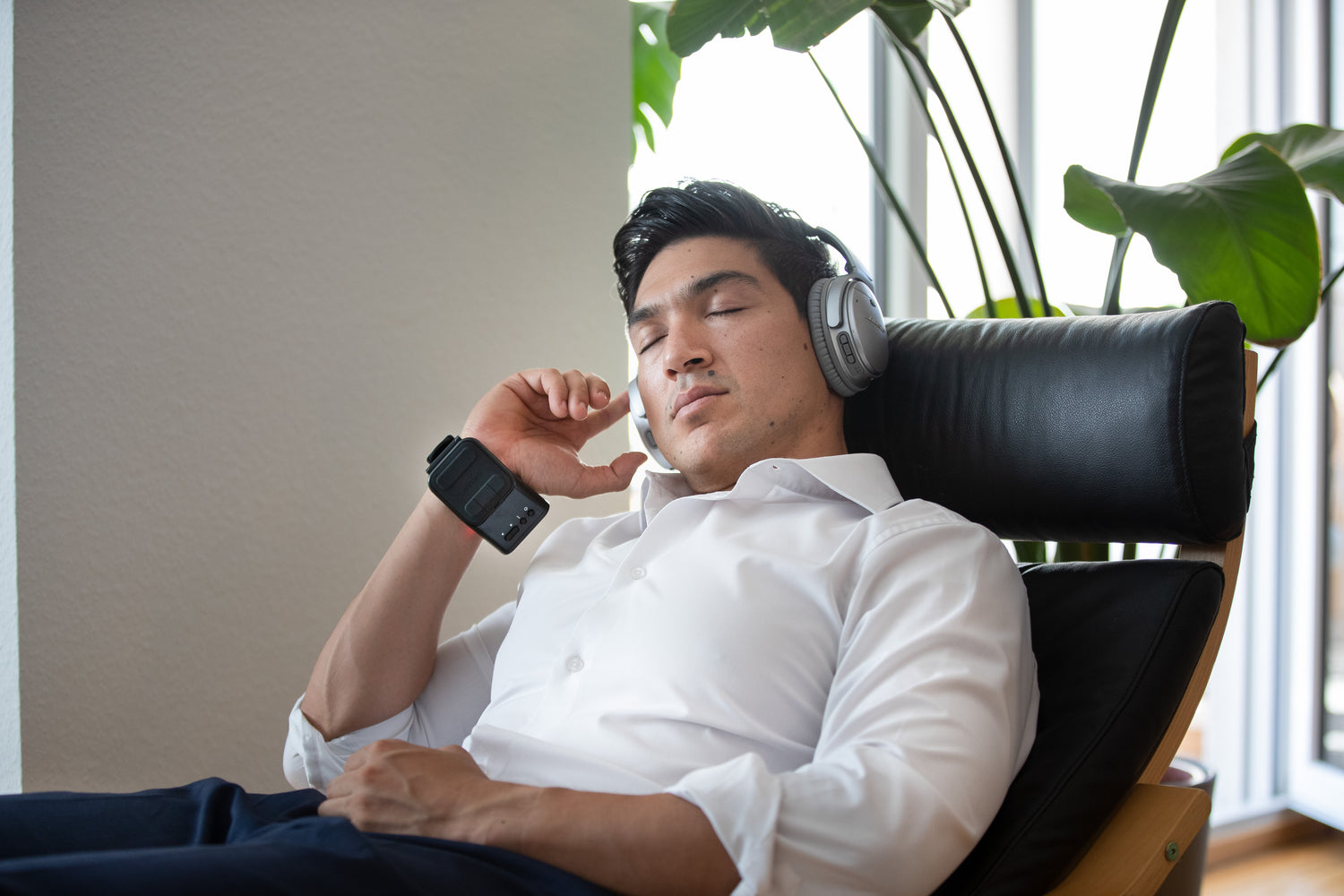Man relaxing in a chair with headphones on, wearing the Weber Medical Endolight Band.